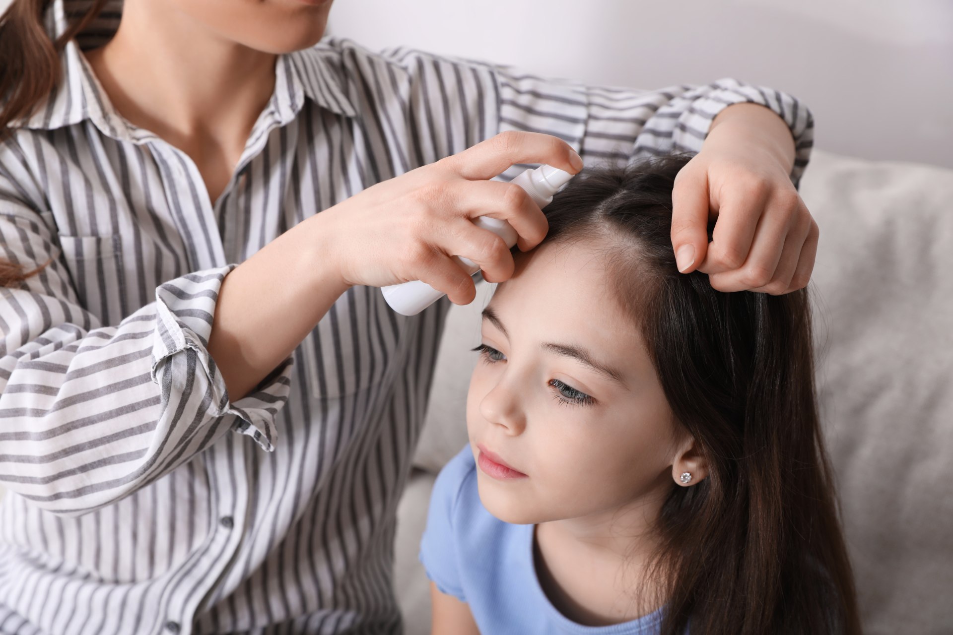 Mujer aplica spray antipiojos en el pelo de una niña